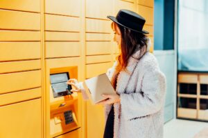 Fashion woman with box using modern postal automatic mail terminal with self service
